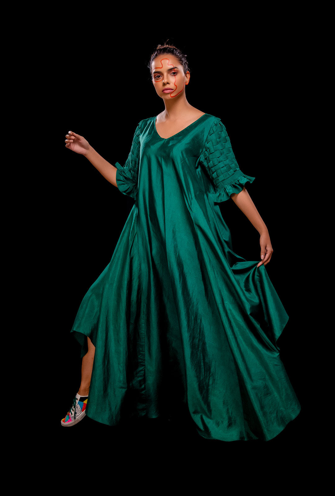 Front view of a green asymmetrical gown with pintuck basket weave sleeve.